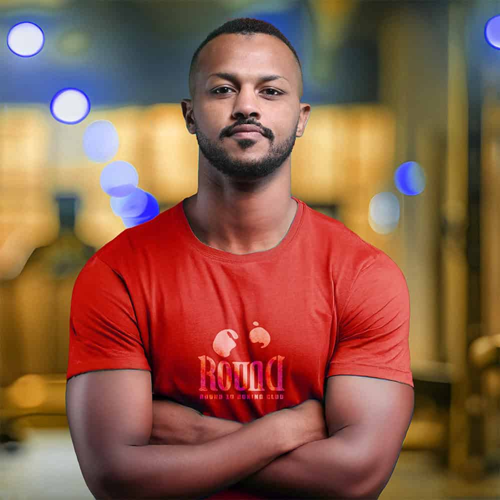 A confident man with short hair and a neat beard stands arms crossed, sporting a "ROUND 10 BOXING CLUB" tee in our Dubai gym.