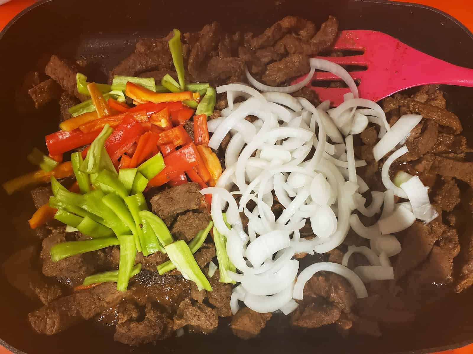 a skillet full of beef fajita meat with sliced onions and peppers on top.
