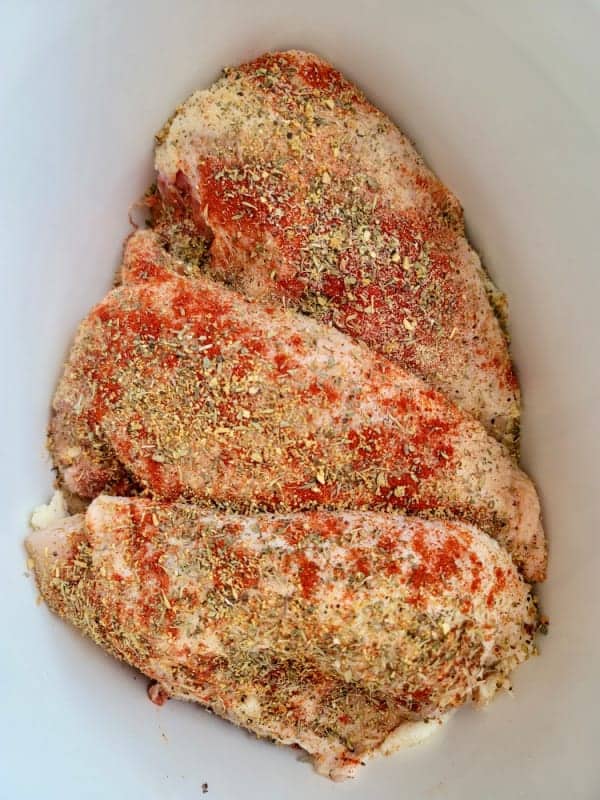 Raw split chicken breasts in a slow cooker.