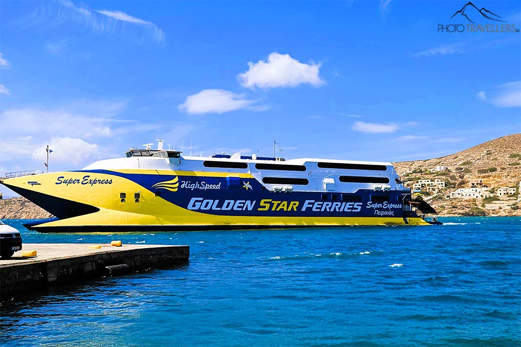 Ein großer, gelb-blauer Katamaran fährt in den Hafen von Ios ein
