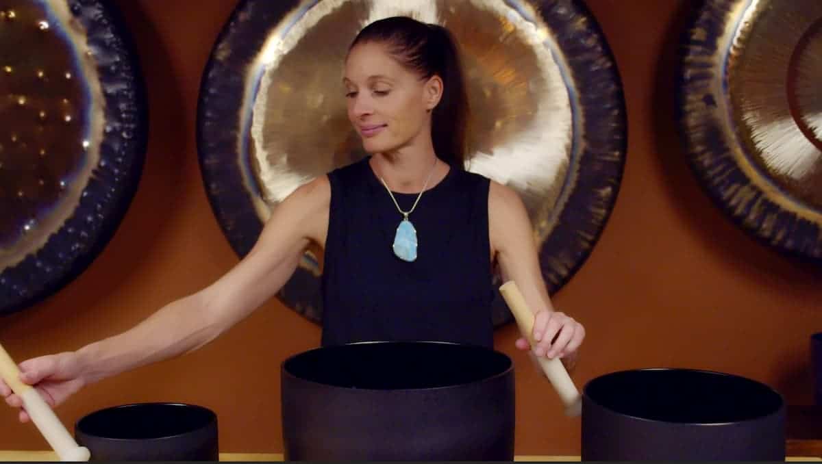 Jamie Bechtold playing two black crystal singing bowls in front of gongs at The Gong Room