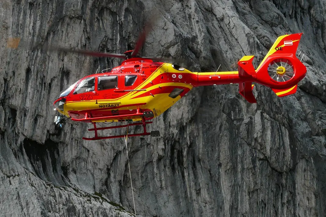 Ein roter Notarzt-Hubschrauber in der Luft vor einer Felswand