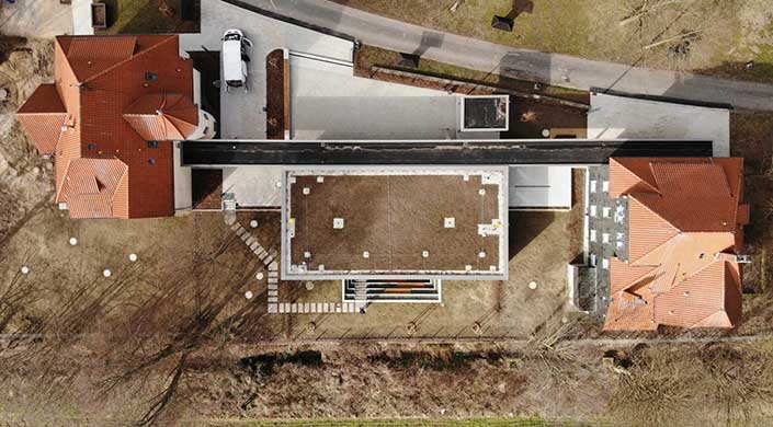 Luftaufnahme eines modernen Gebäudes mit Flachdach, umgeben von Straßen und Rasenflächen, mit klaren Linien und rechteckigem Design.