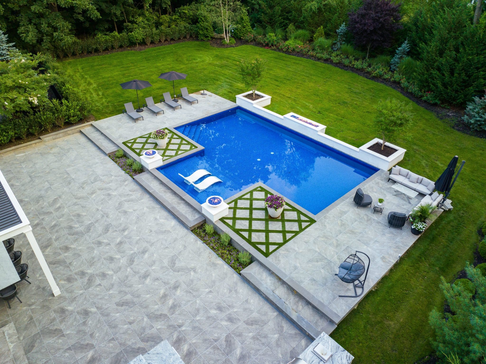 Aerial view of a modern backyard with a rectangular pool, lounge chairs, green lawn, seating areas, and geometric landscaping.