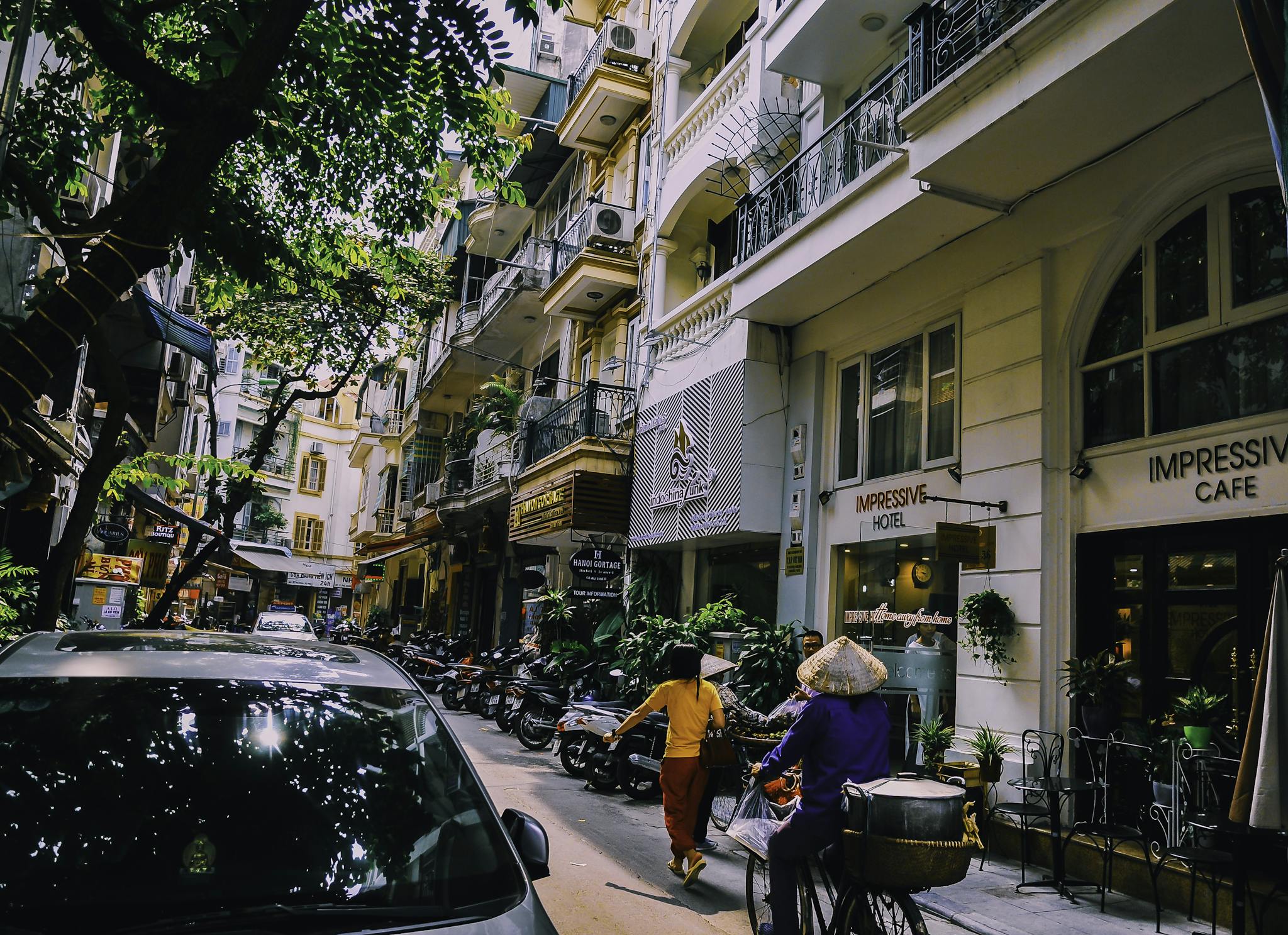 Vibrant street life in Hanoi with locals, cafes, and motorbikes on a sunny day.