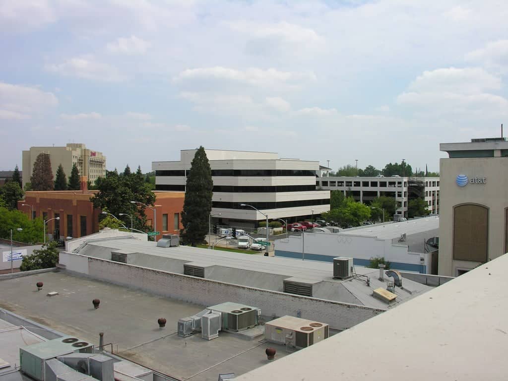 A downtown street in Visalia, California, with two- and three-story storefronts, street trees and parked cars under a blue sky.