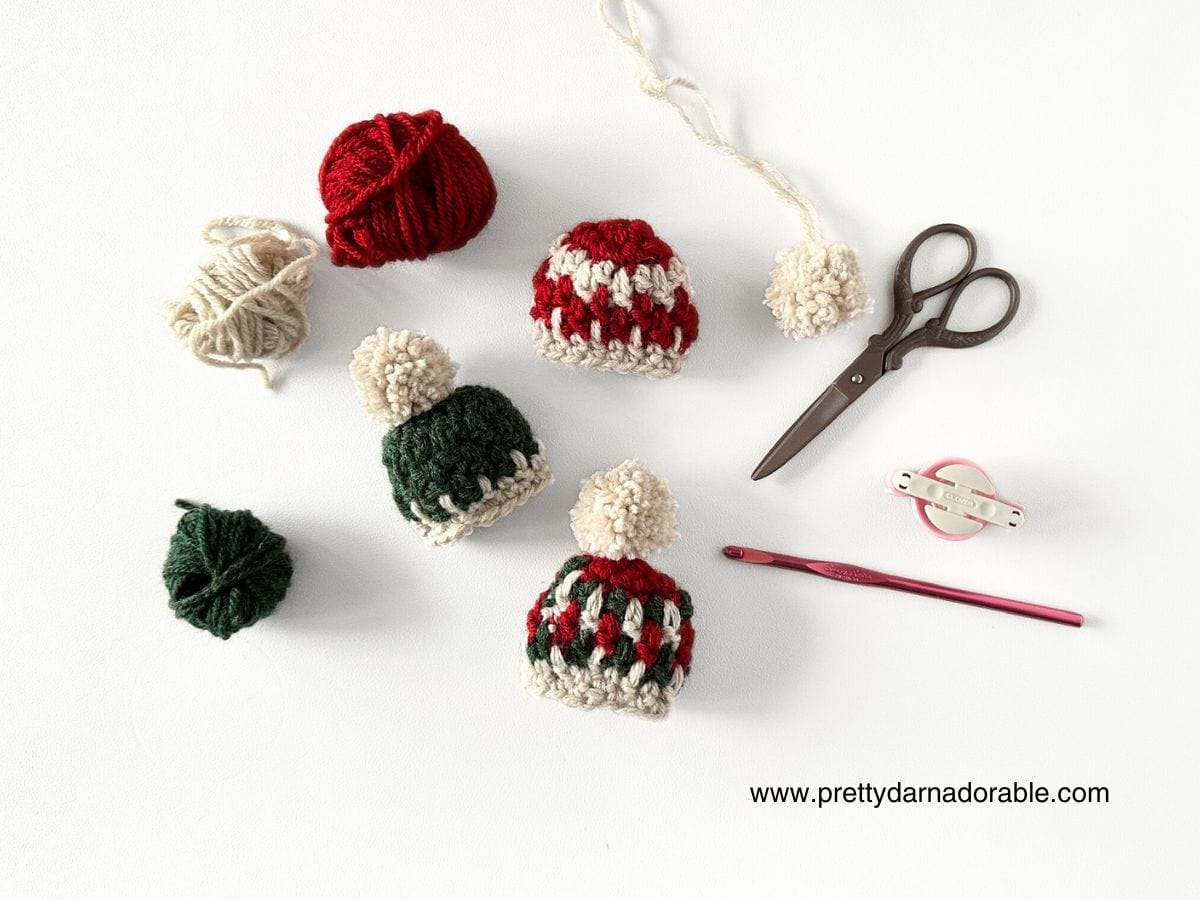 three mini crochet hat ornaments for christmas in red green and white scissors and yarn