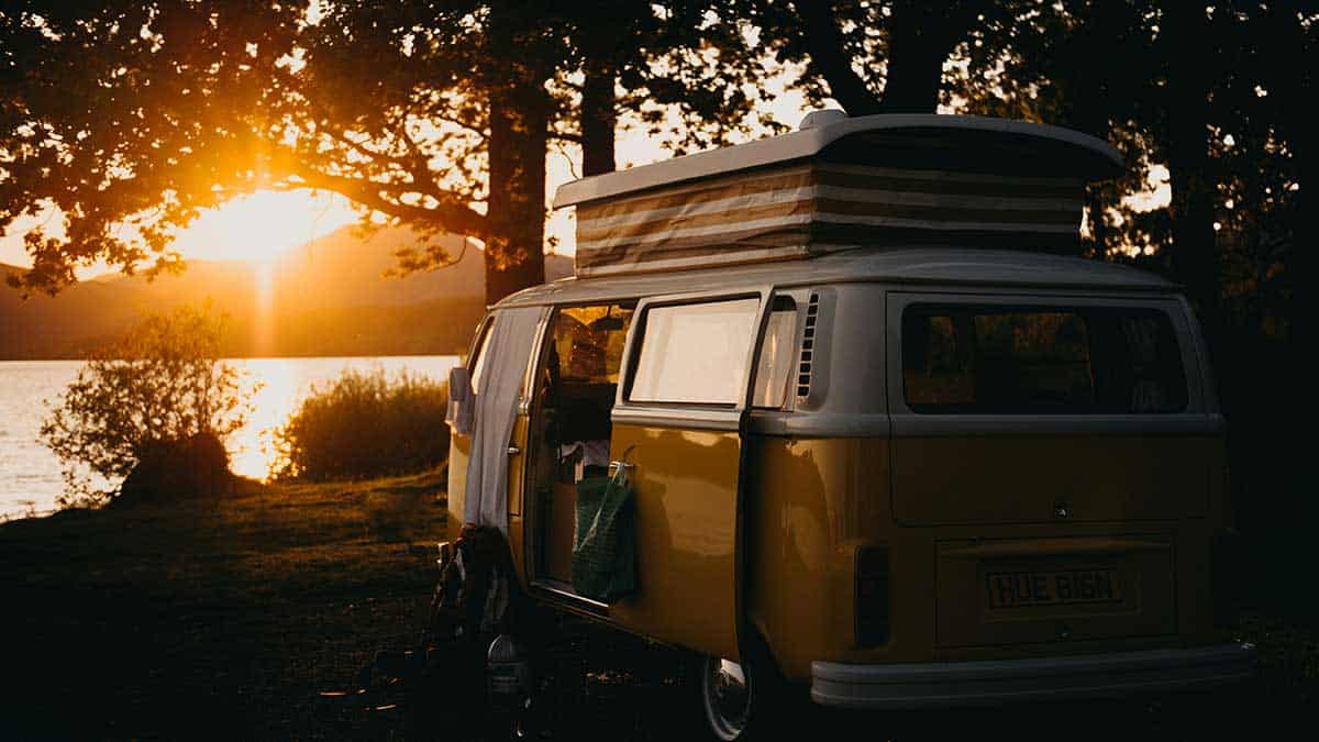 Das Bild zeigt einen Campingwagen vor einem See und Sonnenuntergang