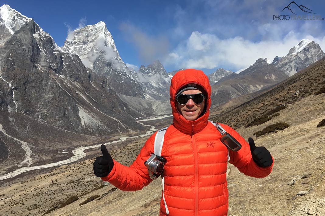 Reiseblogger Florian Westermann in einer orangen Daunenjacke in einem Hochlandtal in Nepal, dahinter hohe Berge