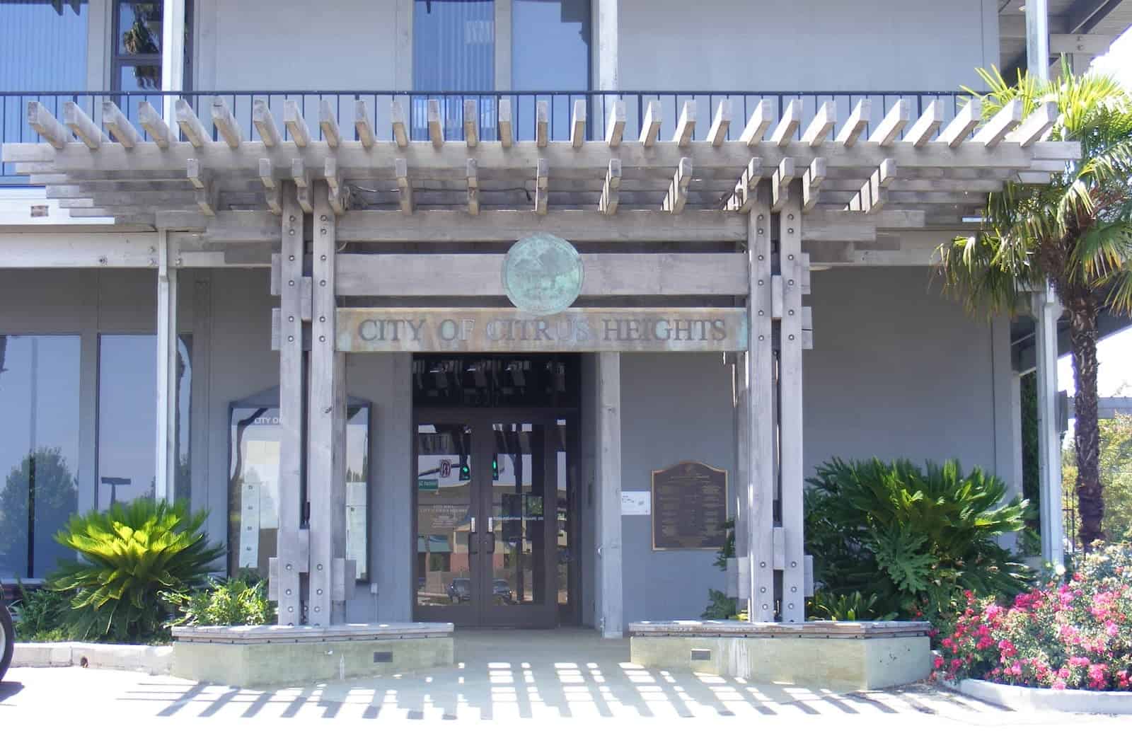 Citrus Heights City Hall, a two-story building with white trellises and columns at its entrance, surrounded by landscaping.