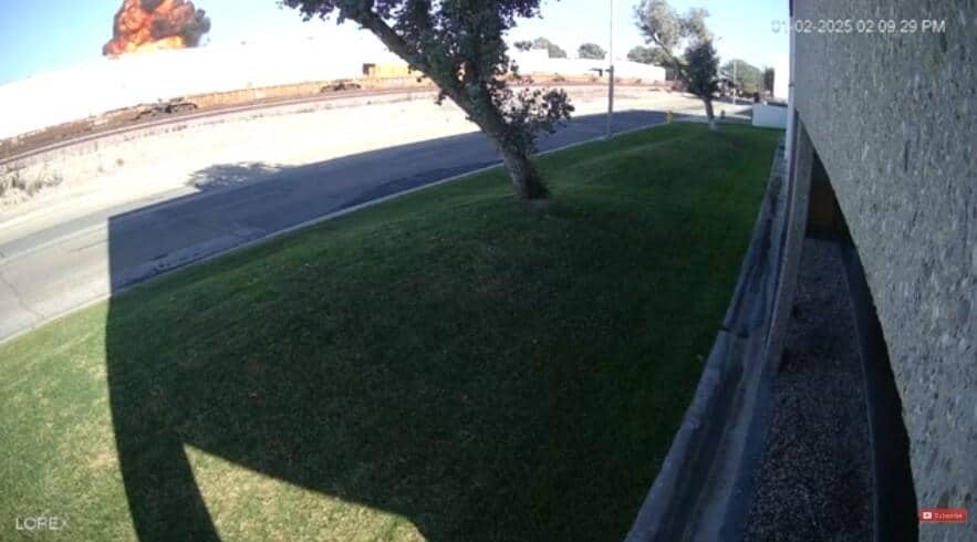 An aerial view captures the aftermath of a plane crash, with a massive explosion billowing smoke over a warehouse in Southern California. The date and time, 01-02-2025 02:09:29 PM, are visible. The Fullerton incident shows the impact of the plane collides with the warehouse.