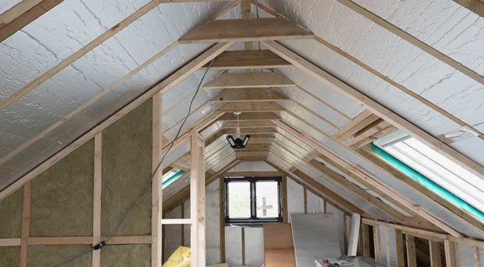 Ein schmaler Dachboden mit sichtbaren Holzträgern, Fenster am Ende und einer Glühbirne an der Decke.