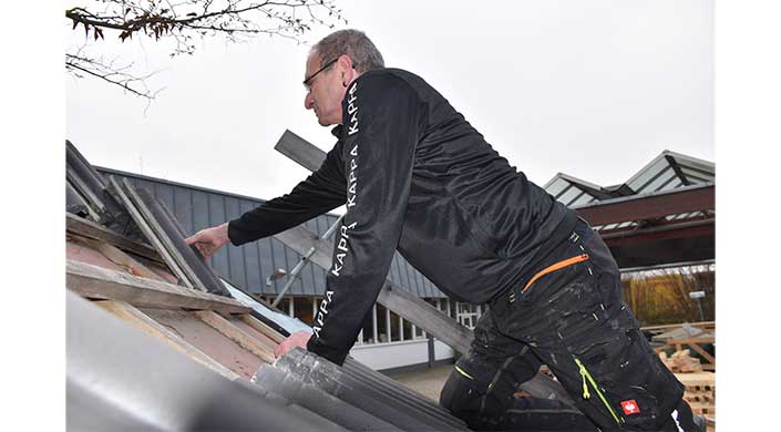 Ein Mann mit Brille und schwarzer KAPPA-Jacke klettert auf eine Metallleiter im Freien neben einem Gebäude.