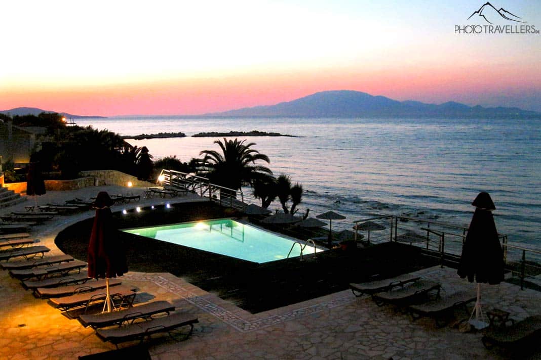 Beleuchteter Hotelpool mit dem Abendrot über dem Meer im Hintergrund