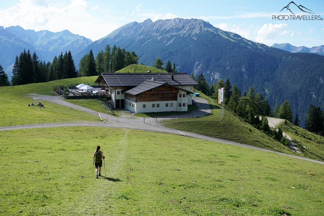 Reisebloggerin Biggi Bauer wandert auf einer Wiese, dahinter ist die Sunnalm zu sehen