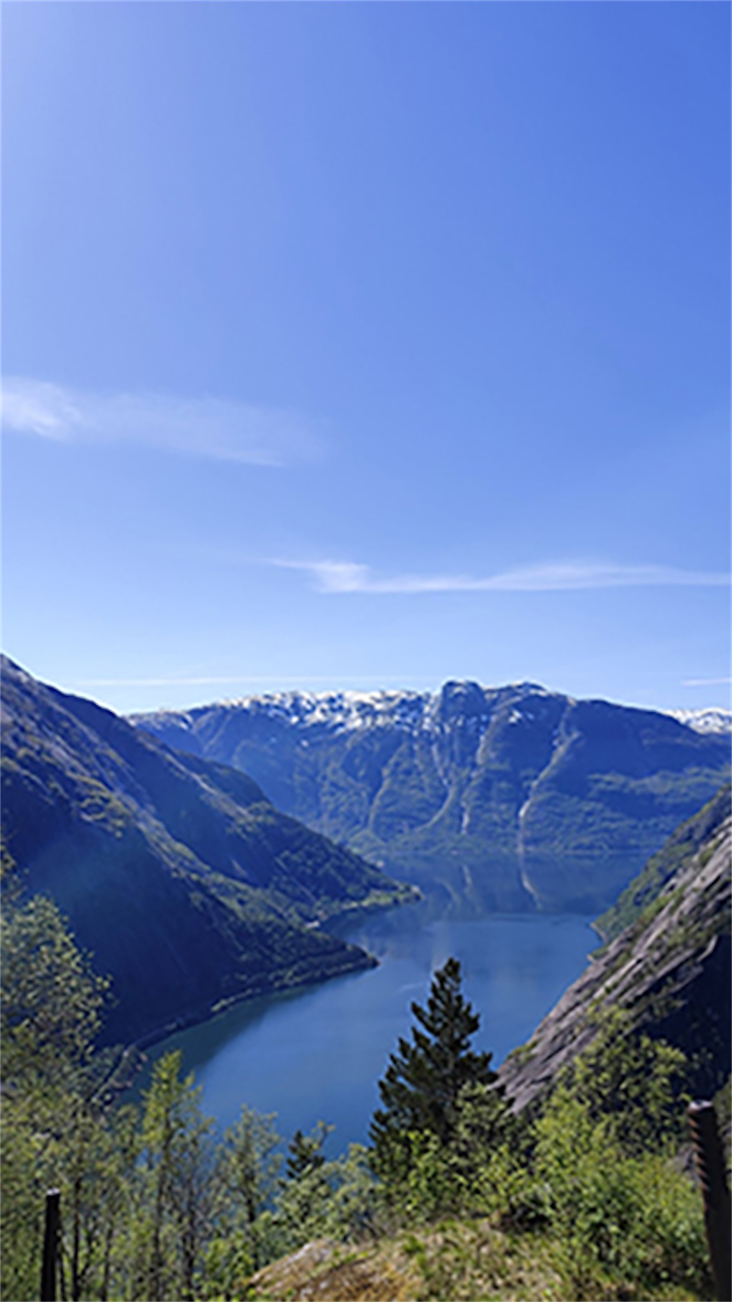 Blick auf einen blauen See, umgeben von Bergen mit Schneegipfeln und klarem, blauem Himmel im Hintergrund.