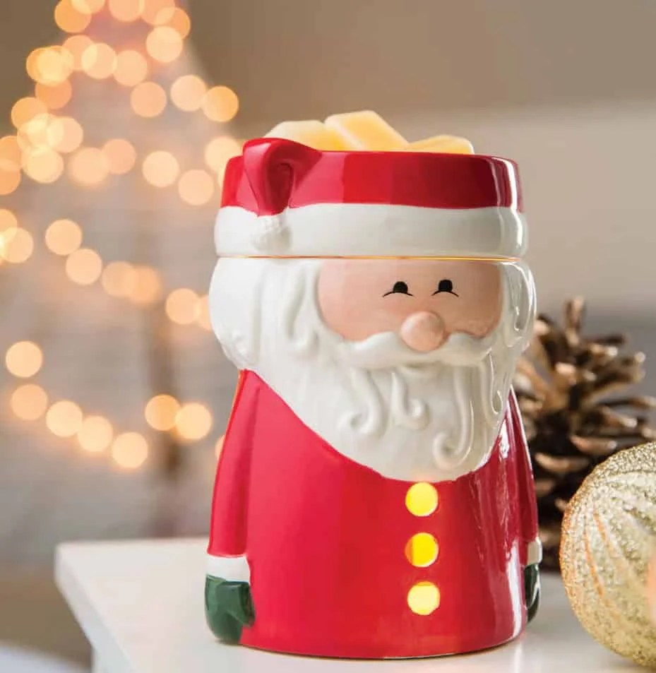 Christmas Gmones in Lights Classic T-Shirt 7 A Santa Claus Wax Warmer sits on a white surface. In the background, blurred holiday lights, a gold ornament, and a pinecone evoke the cozy spirit of Christmas.