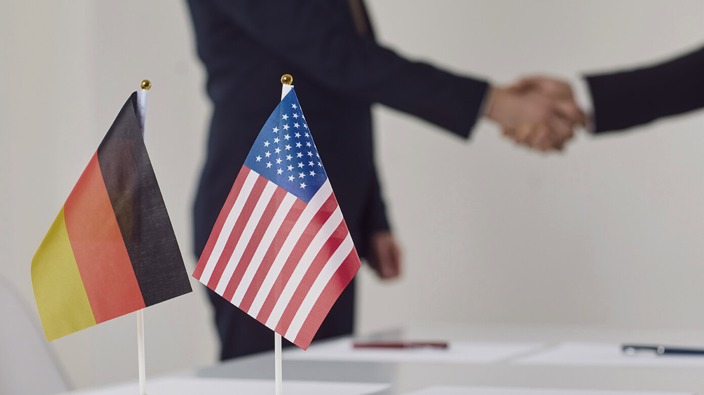 Deutsch-amerikanische Geschäftskooperation mit Handschlag vor Deutschland- und USA-Flaggen Deutsch-amerikanische Geschäftskooperation mit Handschlag vor Deutschland- und USA-Flaggen