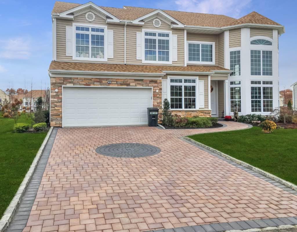 A two-story suburban home with a large front yard, a two-car garage, and a paved driveway under a clear blue sky.
