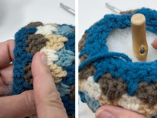 Close-up of hands stuffing a crocheted acorn with blue, beige, cream, and brown colors and a wooden stem in the center. Free crochet pattern