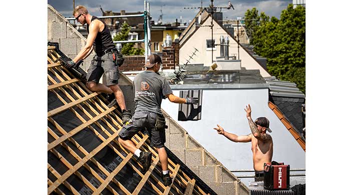 Die Mitarbeiter sollen mit Freude im Betrieb arbeiten Ein Handwerker arbeitet auf einem Dach, trägt Dachziegel und ist auf einer Holzleiter. Im Hintergrund sind Hausdächer und Fernsehantennen zu sehen.