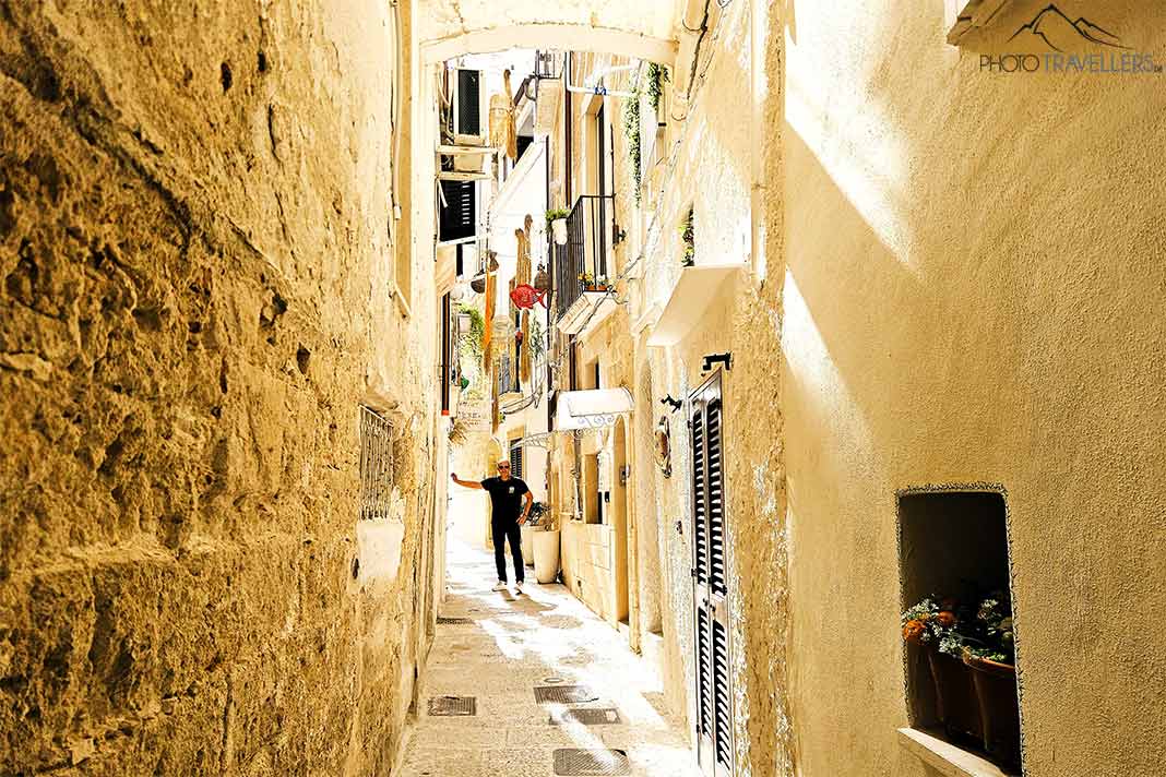 Ein schwarz gekleideter Mann läuft durch eine Licht durchflutete Gasse der Altstadt von Brindisi