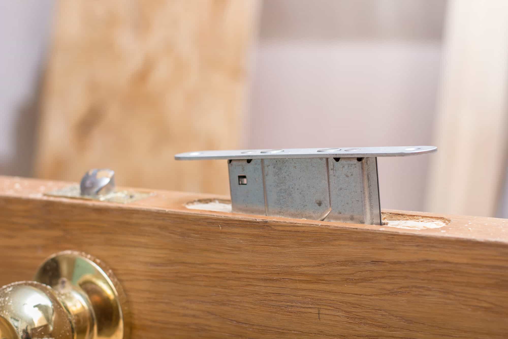 A partially installed door lock mechanism is shown embedded in a wooden door. The copper-colored doorknob contrasts beautifully with the wood. It's clear that a skilled locksmith is in the middle of the door installation or repair process.