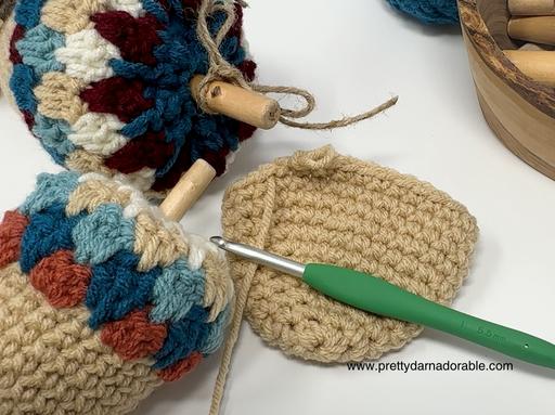 Colorful crocheted acorns with wooden stems and a beige crochet project with green-handled hook on a white surface. Free crochet pattern