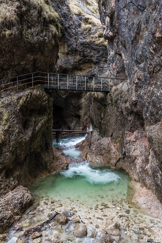 Eine Stahlbrücke in der Almbachklamm, darunter ein kleiner Wasserfall