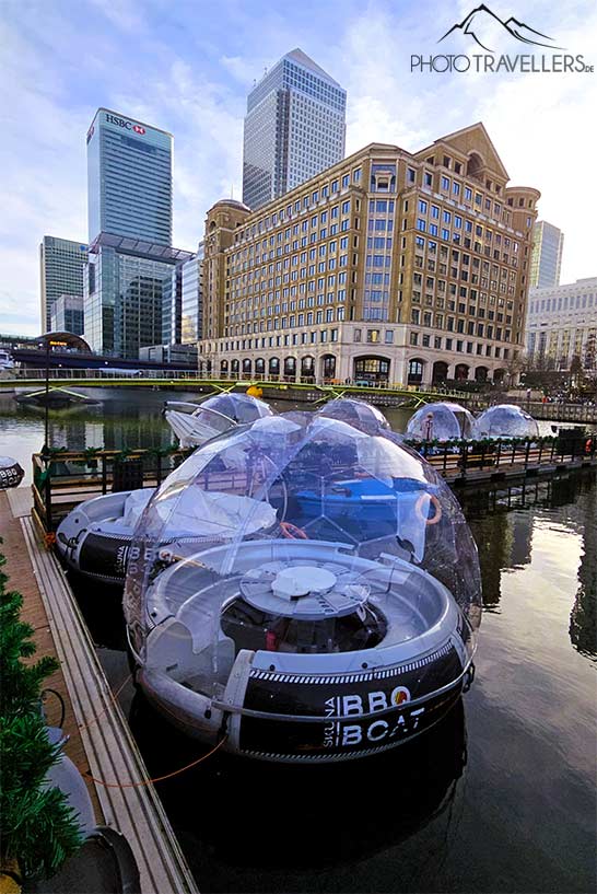 Mehrere schwimmende Iglus mit Glaskuppeldach liegen im Kanal vor den Hochhäusern der Canary Wharf