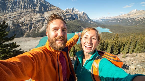 Young couple hiking reaches view point and takes a selfie portrait.