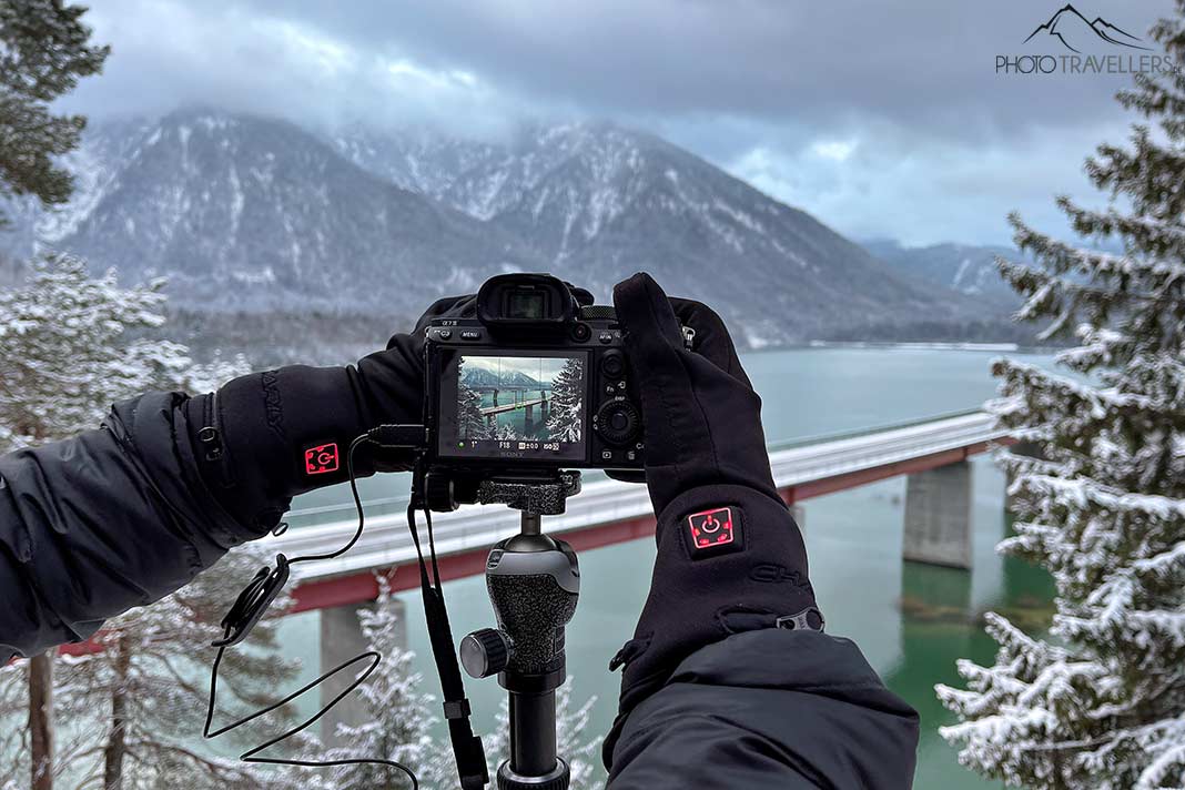 Die beheizten Handschuhe Charly Fire Basic im Einsatz an einer Kamera mit Blick auf einen Bergsee im Winter