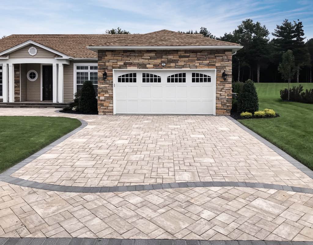 A suburban house featuring a stone facade and attached two-car garage, with a curved paver driveway and manicured lawn.
