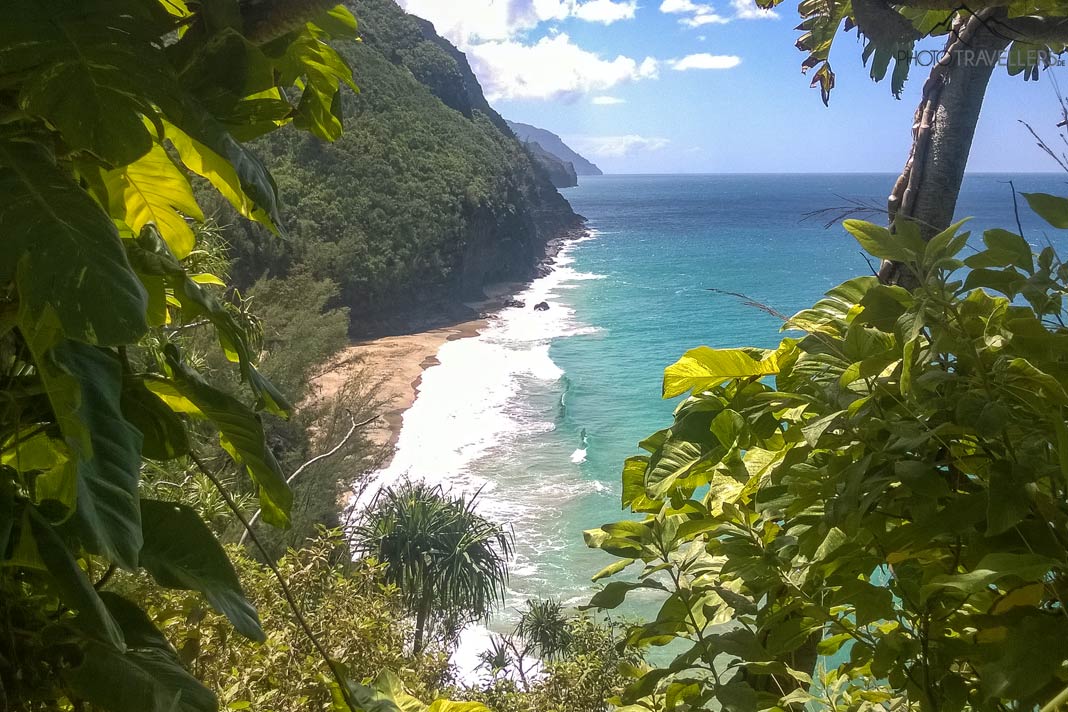 Der Blick vom Kalalau Trail durch Blätter auf den Hanakapiai Beach mit dem türkisen Meer