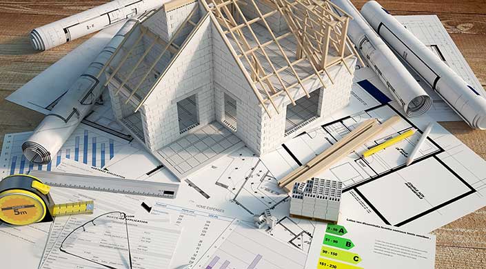 Ein Architekturmodell eines Hauses mit offenem Dach, Bauplänen und Diagrammen auf einem Tisch.
