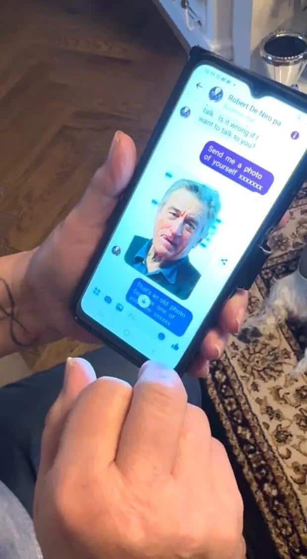 A person's hands hold a smartphone displaying a Facebook Messenger conversation with a "Robert De Niro" profile. The profile picture is of Robert De Niro. Text bubbles show messages like "Send me a photo of yourself" and a reply: "That's an old photo." This is a humorous example of a Robert De Niro scam on Facebook.
