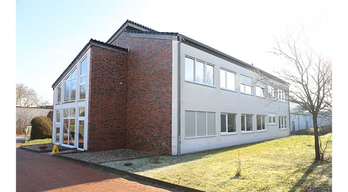 Bild von Gebäude des Instituts für Ziegelforschung Zweistöckiges Gebäude mit roter Klinkerfassade an der Seite und weißen Wänden vorne, großen Fenstern und Rasen im Vordergrund.