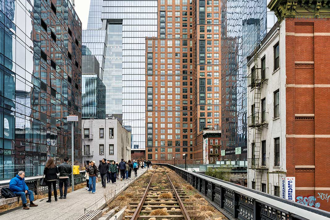 Besucher spazieren auf der High Line neben einem alten Gleis zwischen Wolkenkratzern in New York