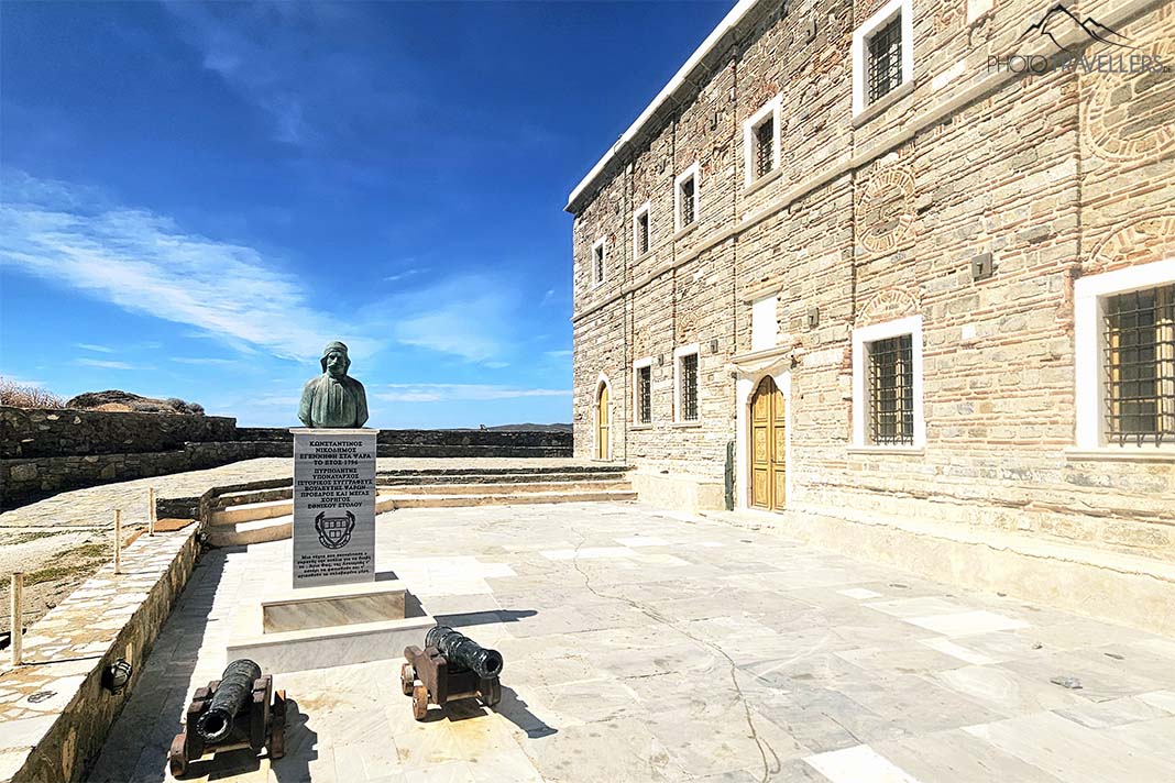 Seitenansicht der zweistöckigen Steinkirche Agios Nikolaos mit Denkmal von Konstantinos Nikodimos daneben