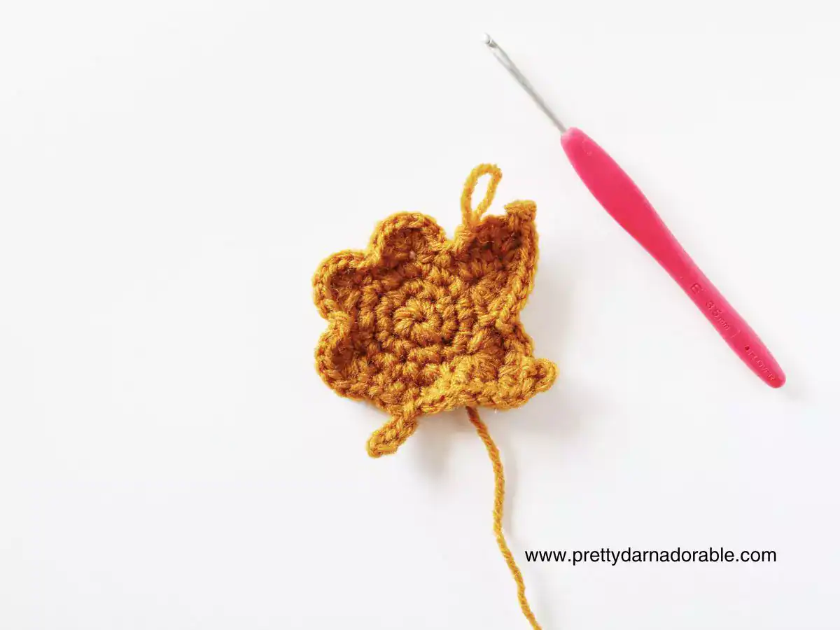 Yellow crocheted maple leaf with loose yarn end beside pink crochet hook on white background; www.prettydarnadorable.com in corner. Free crochet pattern