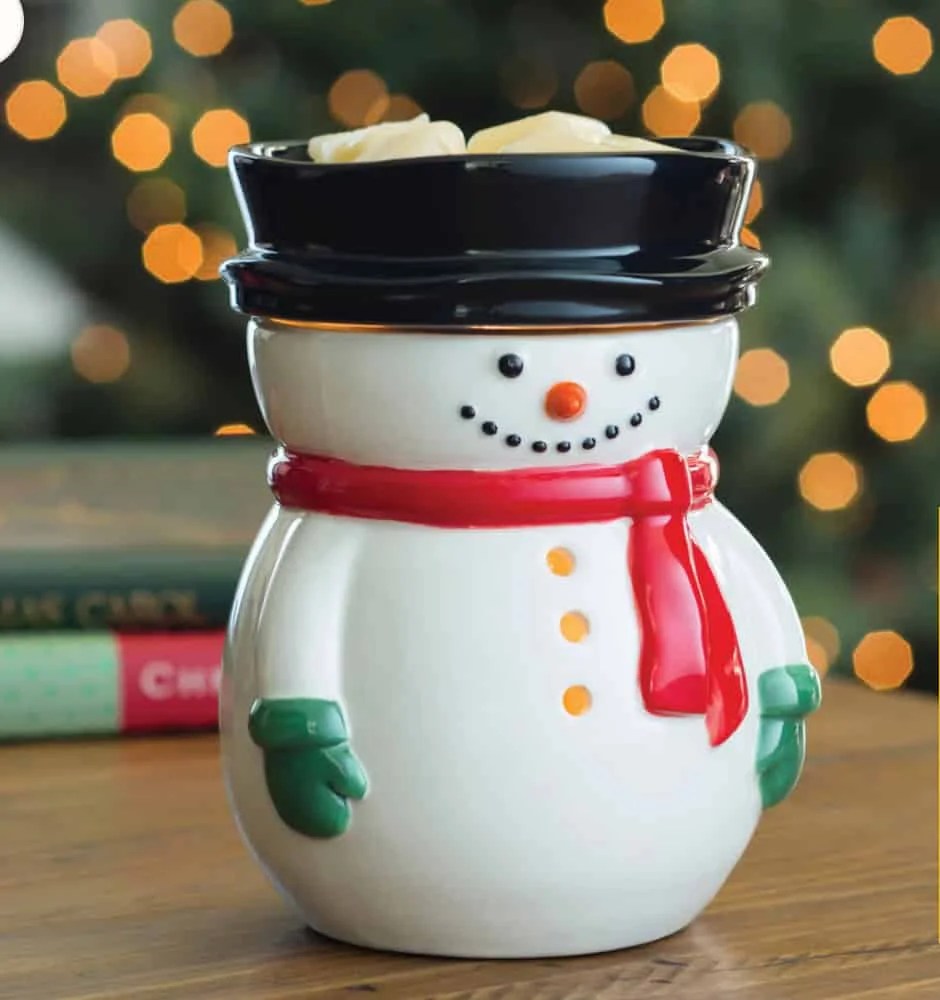 Christmas Gmones in Lights Classic T-Shirt 4 A Frosty Snowman Wax Warmer with a red scarf, green mittens, and black hat sits on a wooden table. The background shows blurred holiday lights and books.