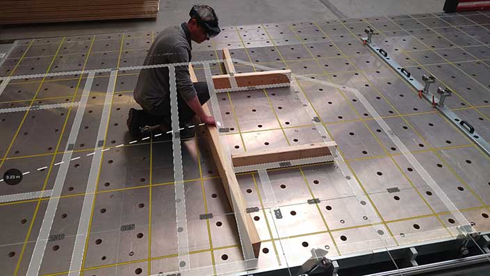Person arbeitet an einer Arbeitsplatte mit Holzlatten und Metallwinkeln, vermutlich für präzise Messungen oder Zusammenbau.