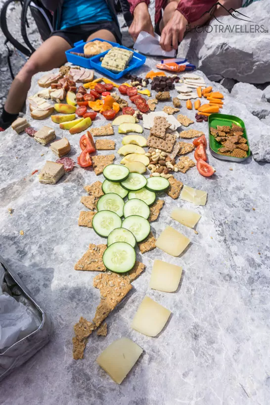 Knäckebrot, Käse und Gemüse ausgebreitet auf einem Fels an einem Gipfel