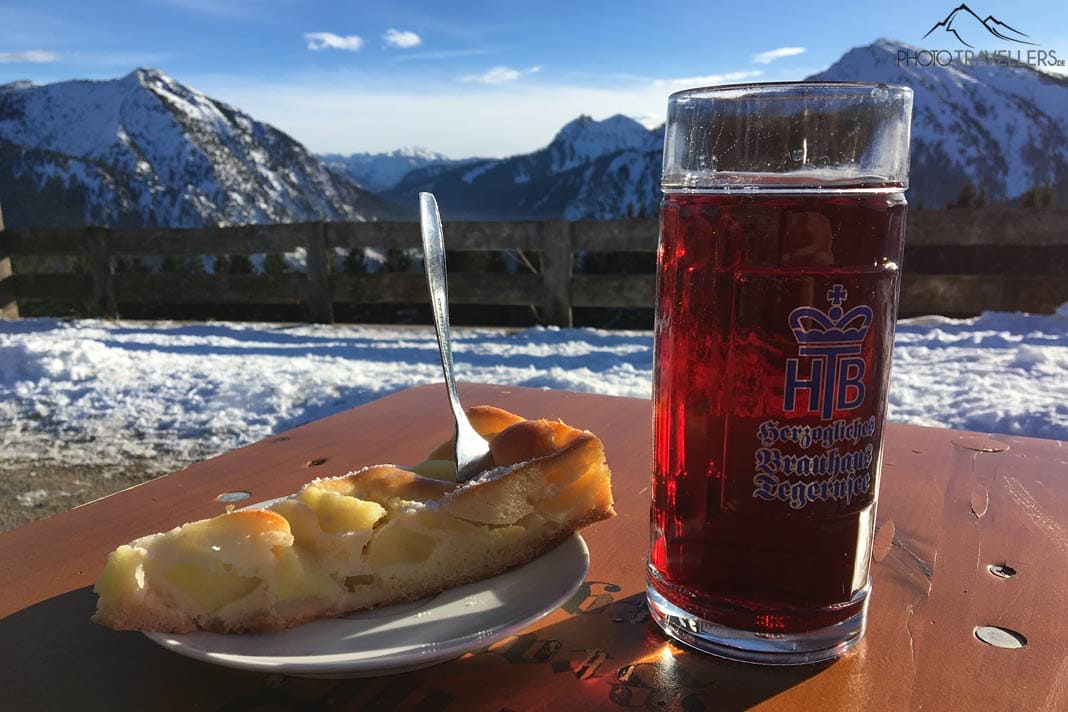 Ein Apfelkuchen mit einer Saftschorle auf der Aueralm mit Blick in die verschneiten Berge