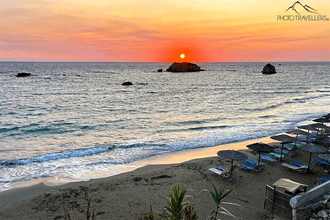 Sandstrand mit Liegen im Sonnenuntergang dahinter Felsen im Meer