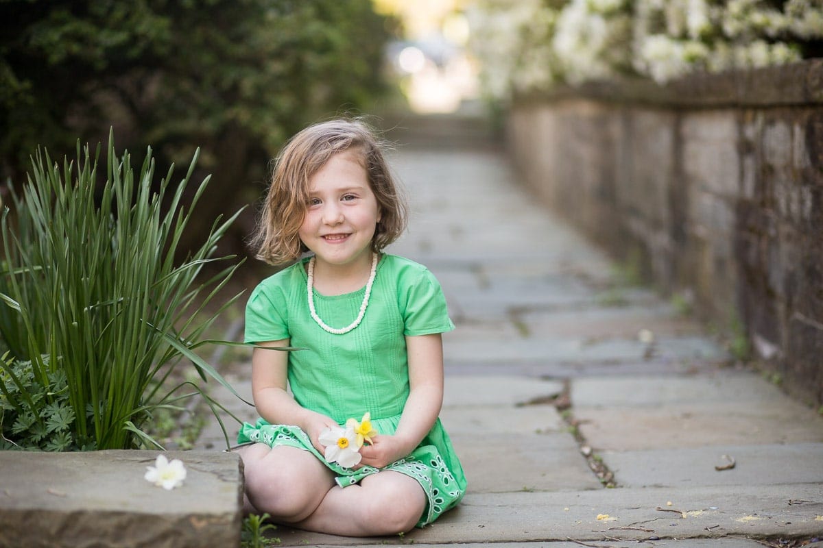 Young girl in green dress holding a flower sits on a stone walkway at Washington National Cathedral