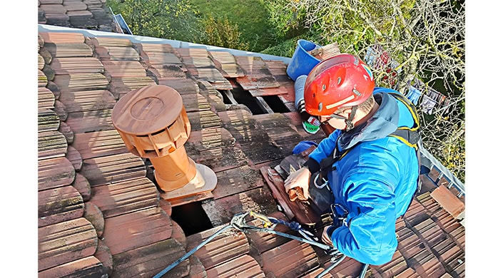 Dachziegel sind beschädigt und fehlen, mit Werkzeugen und Bauausrüstung auf dem Dach; deutliche Anzeichen von Reparaturarbeiten an einem Hausdach.