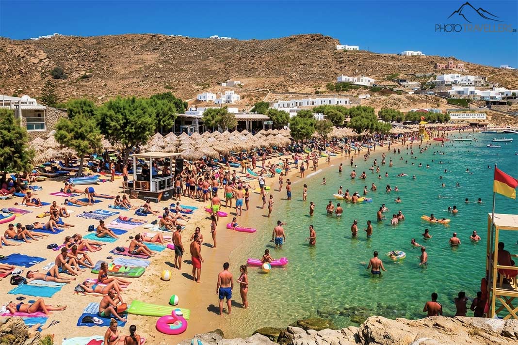 Liegen voller Menschen und Badegäste am grün-blauen Wasser des Paradise Beach auf Mykonos