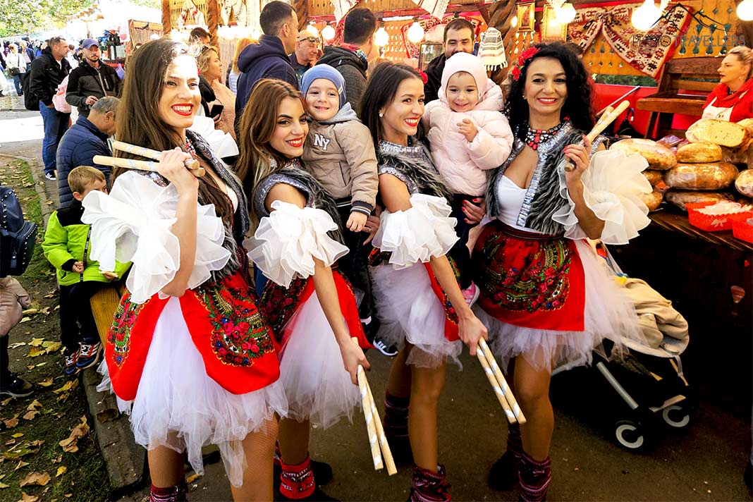 Vier Frauen in rot-weißer Folkloretracht posieren mit Kindern auf einem Markt