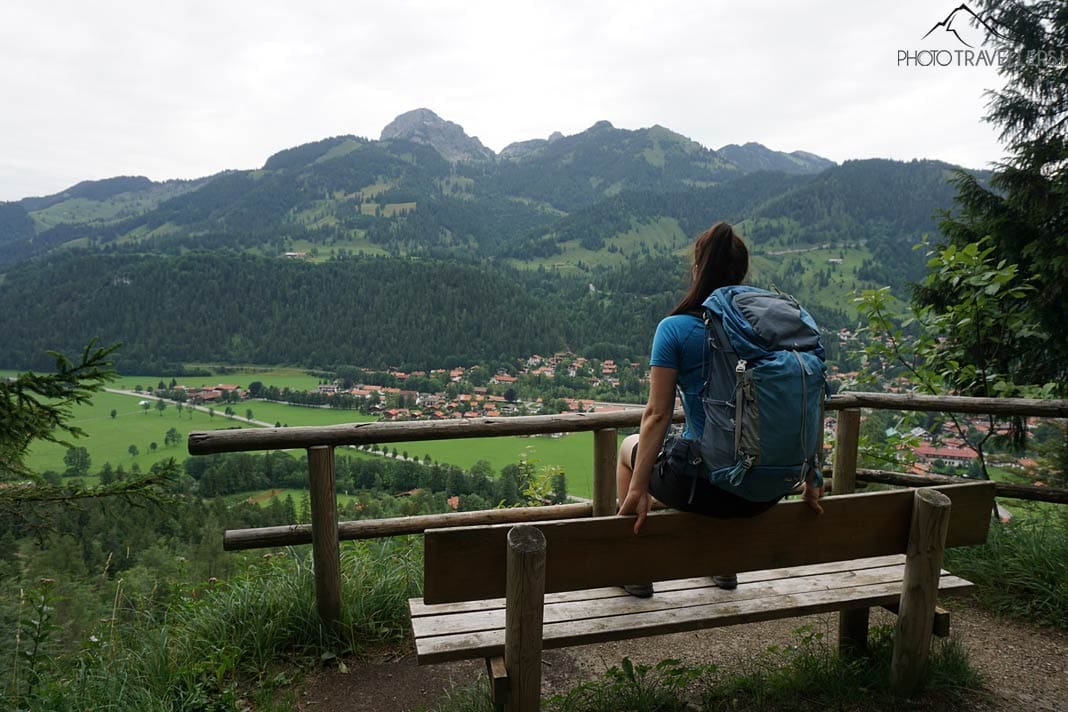 Reisebloggerin Biggi Bauer sitzt auf einer Bank und blickt hinab auf Bayrischzell.
Dahinter ragt der Wendelstein in den Himmel